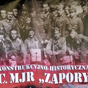 Szaro-czerwone logo GRH przedstawiające grupę mężczyzn z napisem Grupa Rekonstrukcyjno-Historyczna im. cc. mjr "Zapory".