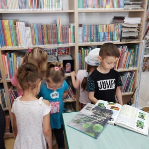 Dzieci biorące udział w zajęciach bibliotecznych w trakcie zapoznawania się z księgozbiorem biblioteki. 