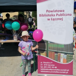 Stojąca dziewczynka przy namiocie PBP w Łęcznej, trzymająca  różowy balon z logo biblioteki w trakcie "II Powiatowego Sportowego Dnia Dziecka".