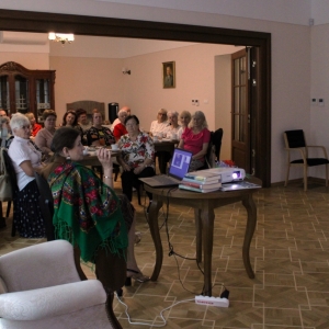 Wnętrze dworu, siedzący seniorzy podczas prezentacji. 